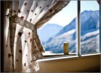 picture of a window because of the curtains open. Sun is shining in to the space and snow-covered mountains tend to be noticeable outside. Copyright Fochesato.
